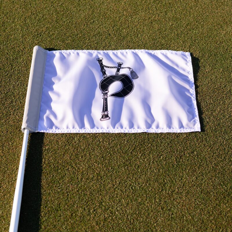 A white pin flag with a black bagpipe logo laid flat on a green