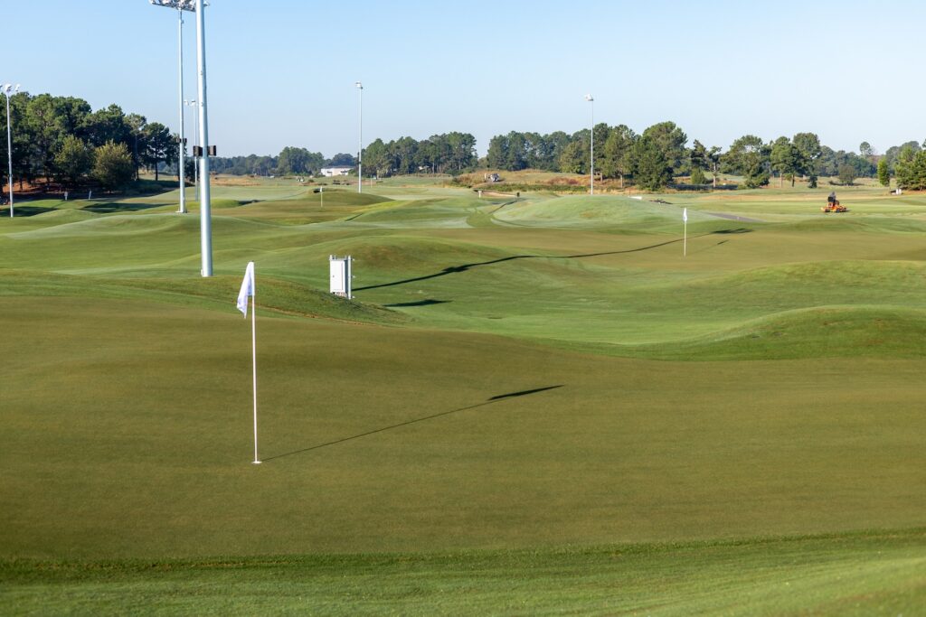 A green on The Piper with a pin flag, rolling mounds behind it and tall light poles against a blue sky
