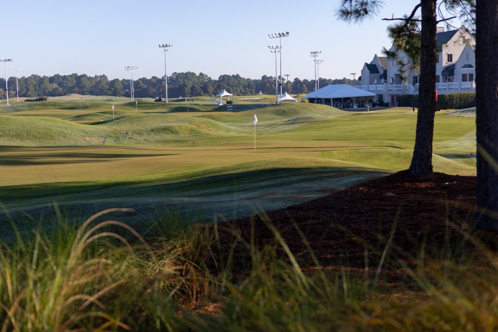 Looking across The Piper through pine trees toward the Legends clubhouse, with event tents set up for the preview