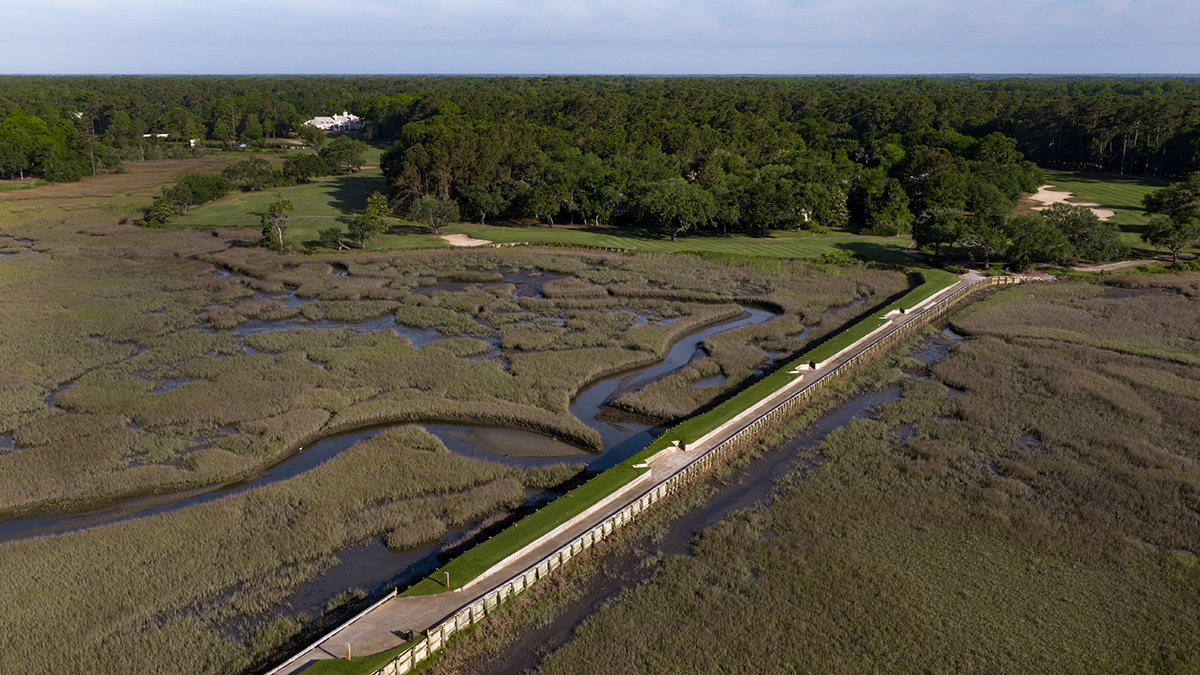 The 17th green at Pawleys Plantation beside a lake with a fountain, with salt marsh and the beach houses of Pawleys Island in the distance